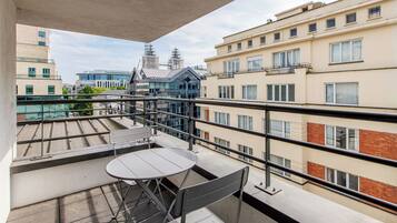 Un balcón con mesa y sillas, con vistas a un paisaje urbano que combina edificios modernos y tradicionales.