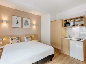 Una habitación de hotel compacta con cama, kitchenette pequeña y televisor montado en la pared.
