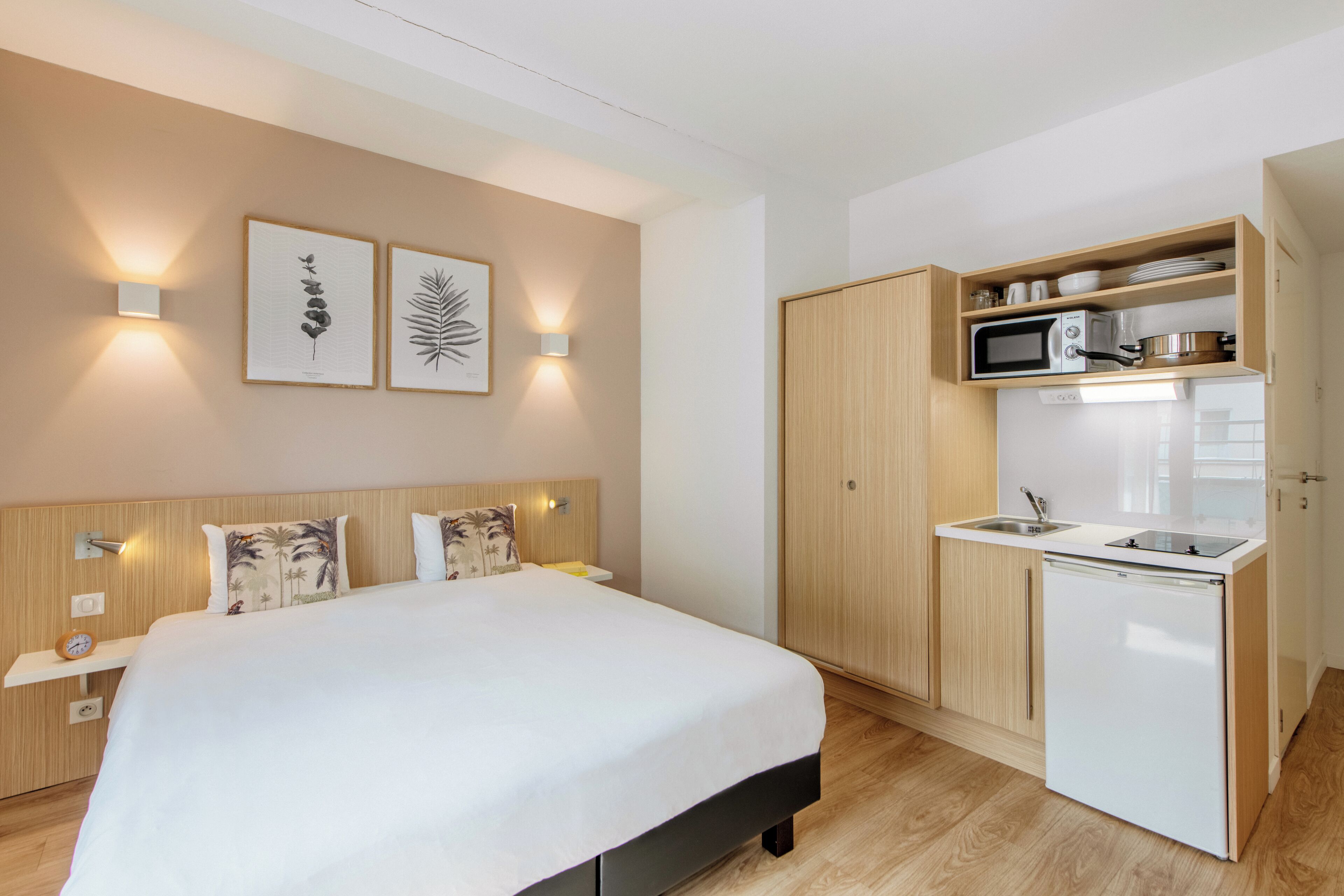 Ein kleines Hotelzimmer mit Bett, Nachttischen, einer kleinen Küchenzeile und einer Wandleuchte.