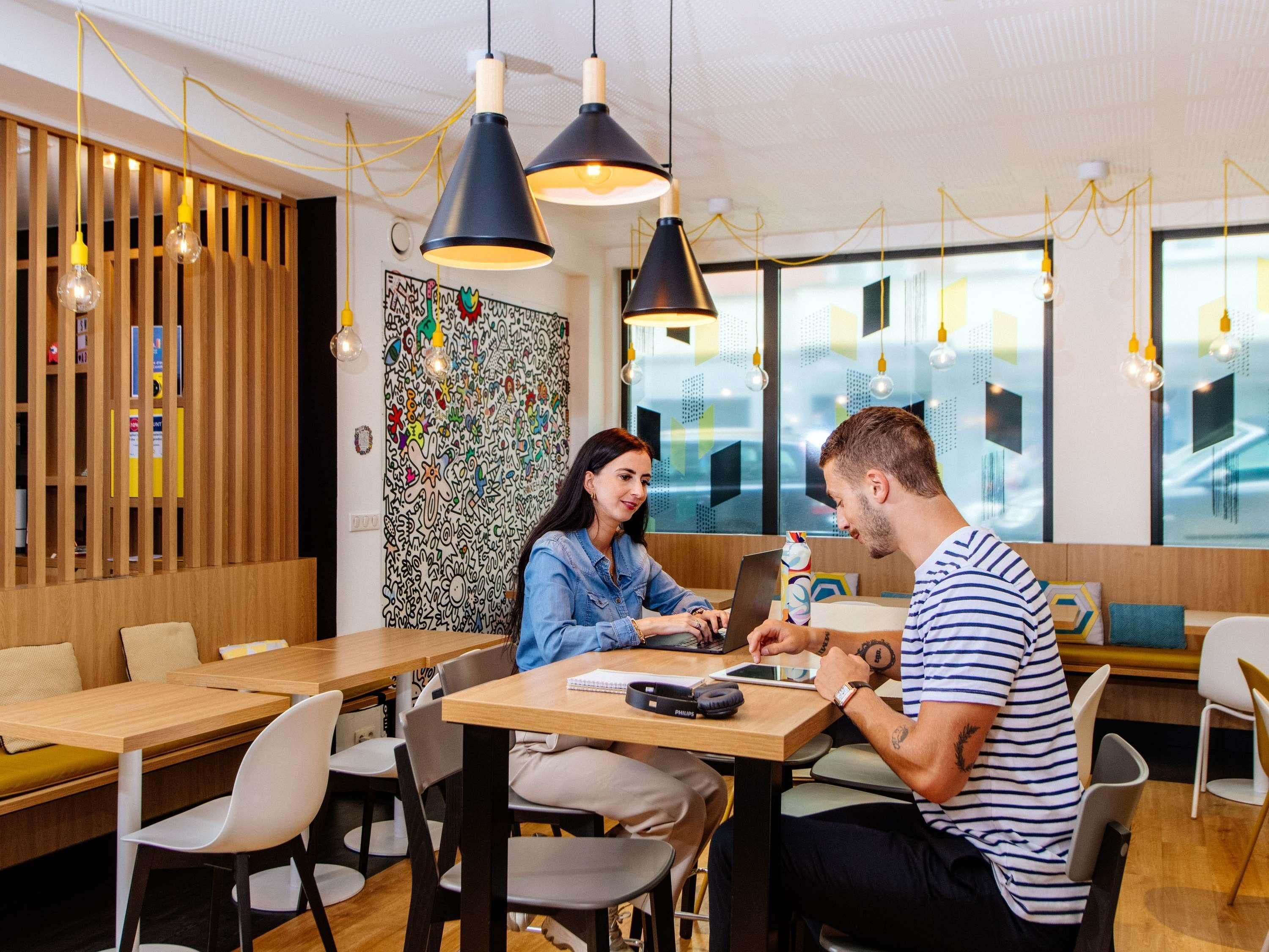 En moderne café med træmøbler, sorte og gule hængelamper og farverigt abstrakt vægkunst.