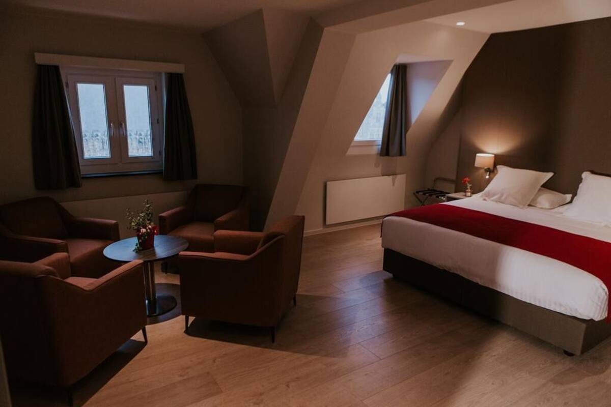 Una habitación de hotel moderna con una cama grande, una mesita redonda y dos sillones.