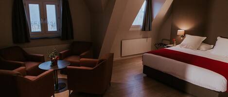 Een moderne hotelkamer met een groot bed, een klein rond tafeltje en twee fauteuils.