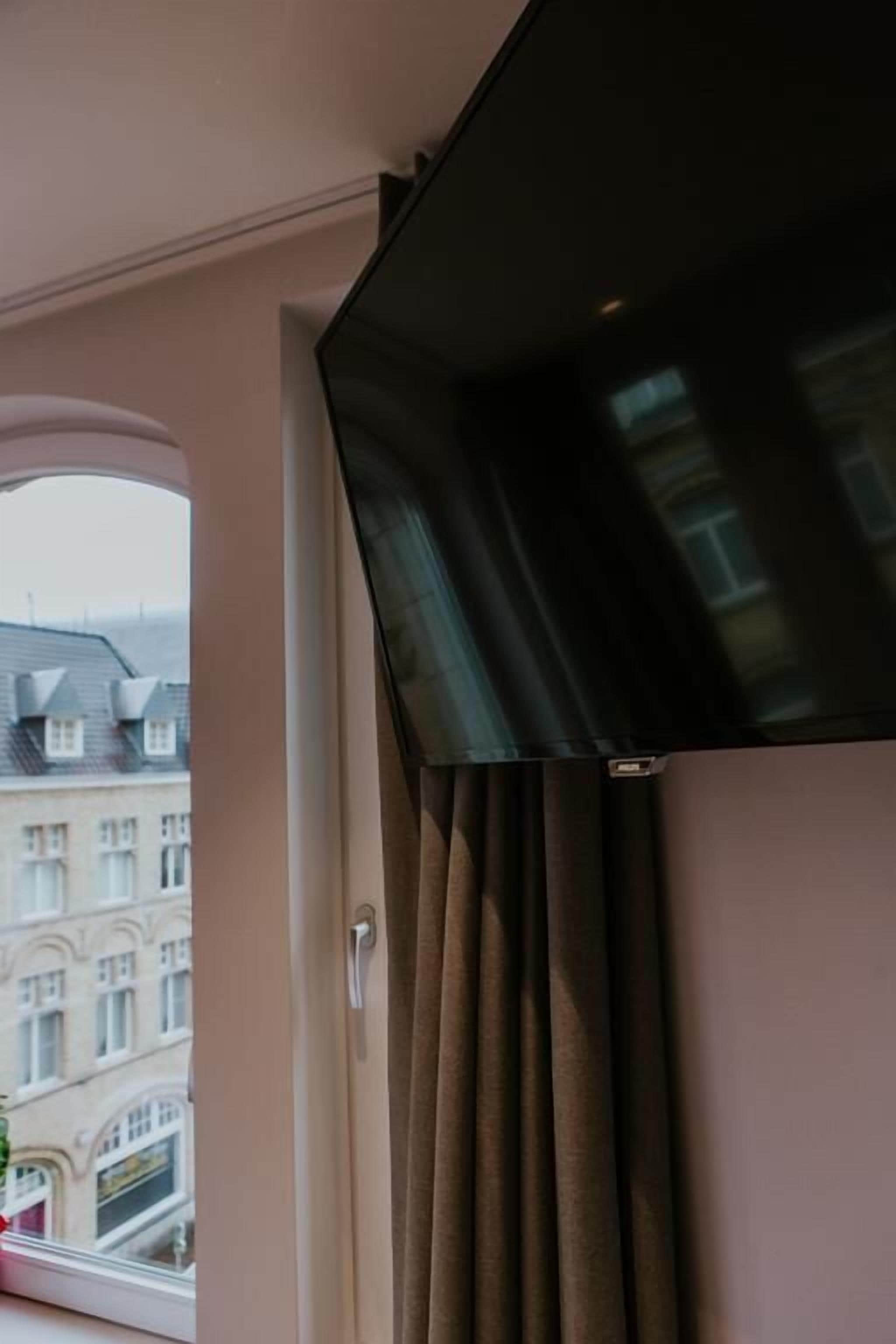 Een kamer met een groot raam, een wandtelevisie en een gordijn.