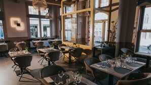 A restaurant interior with multiple tables and chairs, large windows, and modern lighting fixtures. - Hotel New Regina (Ypres)
