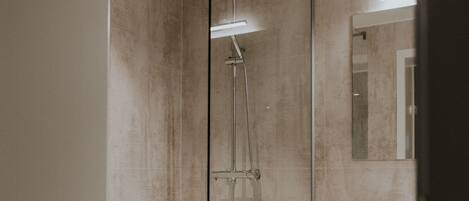 Un baño moderno con ducha envuelta en vidrio, un lavamanos y un espejo.
