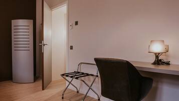 Een moderne kamer met een houten vloer, een zwarte lederen fauteuil, een klein tafeltje met een lamp en een witte deur.