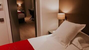 A hotel room with a bed, a nightstand, a lamp, and a door leading to another room.