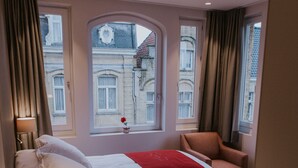 A hotel room with two beds, a chair, a lamp, and a phone on the nightstand. - Hotel New Regina (Ypres)