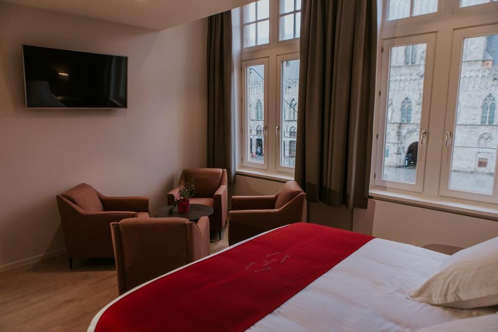 Une chambre d’hôtel avec un lit, un téléviseur fixé au mur et une vue sur un bâtiment historique par la fenêtre.