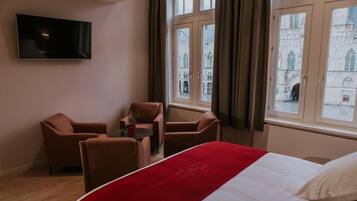 Une chambre d’hôtel avec un lit, un téléviseur fixé au mur et une vue sur un bâtiment historique par la fenêtre.