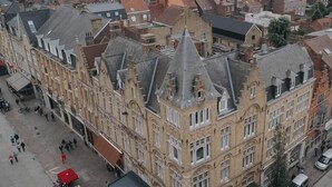 A historic building with a prominent corner turret, a courtyard with outdoor seating, and a pedestrian street. - Hotel New Regina (Ypres)