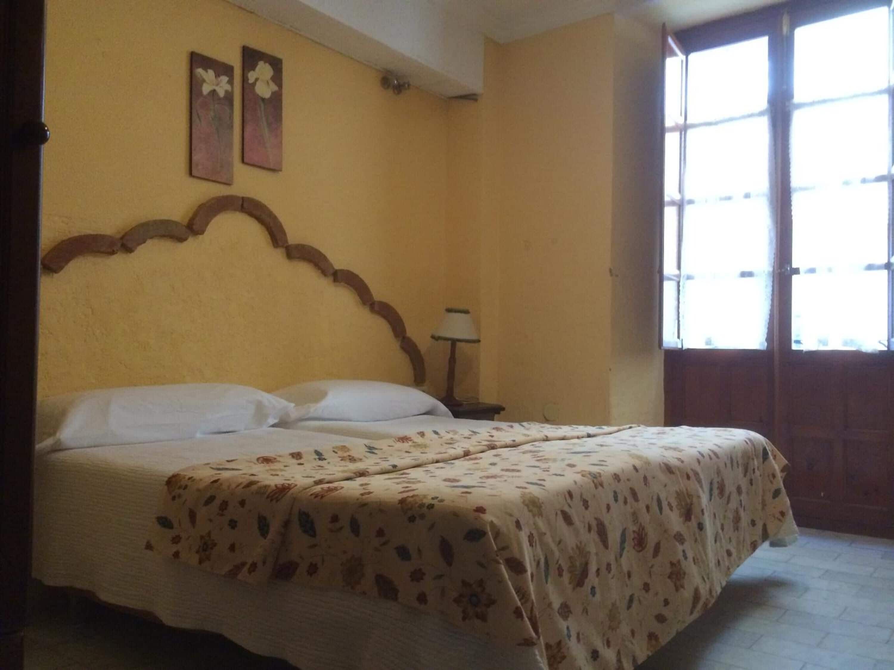 Una cama con colcha estampada de flores, cabecera de madera y dos cuadros de flores colgados en la pared.