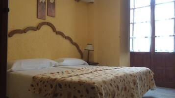 Una cama con colcha estampada de flores, cabecera de madera y dos cuadros de flores colgados en la pared.