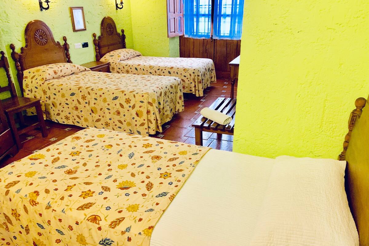 A room with two beds, a wooden bench, and a window with curtains.
