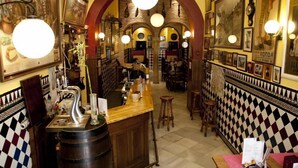 A bar area with a wooden counter, stools, and a large mirror. - Hermanos Macías Hotel (Ronda)