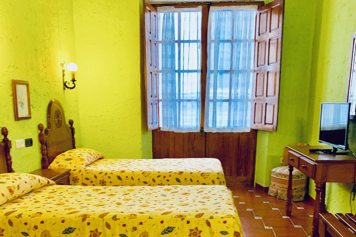 A room with two beds, a desk with a computer, and a window with curtains.