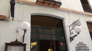 A building entrance with a green door, a sign above the door, and two wall-mounted light fixtures. - Hermanos Macías Hotel (Ronda)