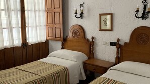 A room with two single beds, wooden headboards, a nightstand, a wall-mounted light fixture, and a window with curtains. - Hermanos Macías Hotel (Ronda)