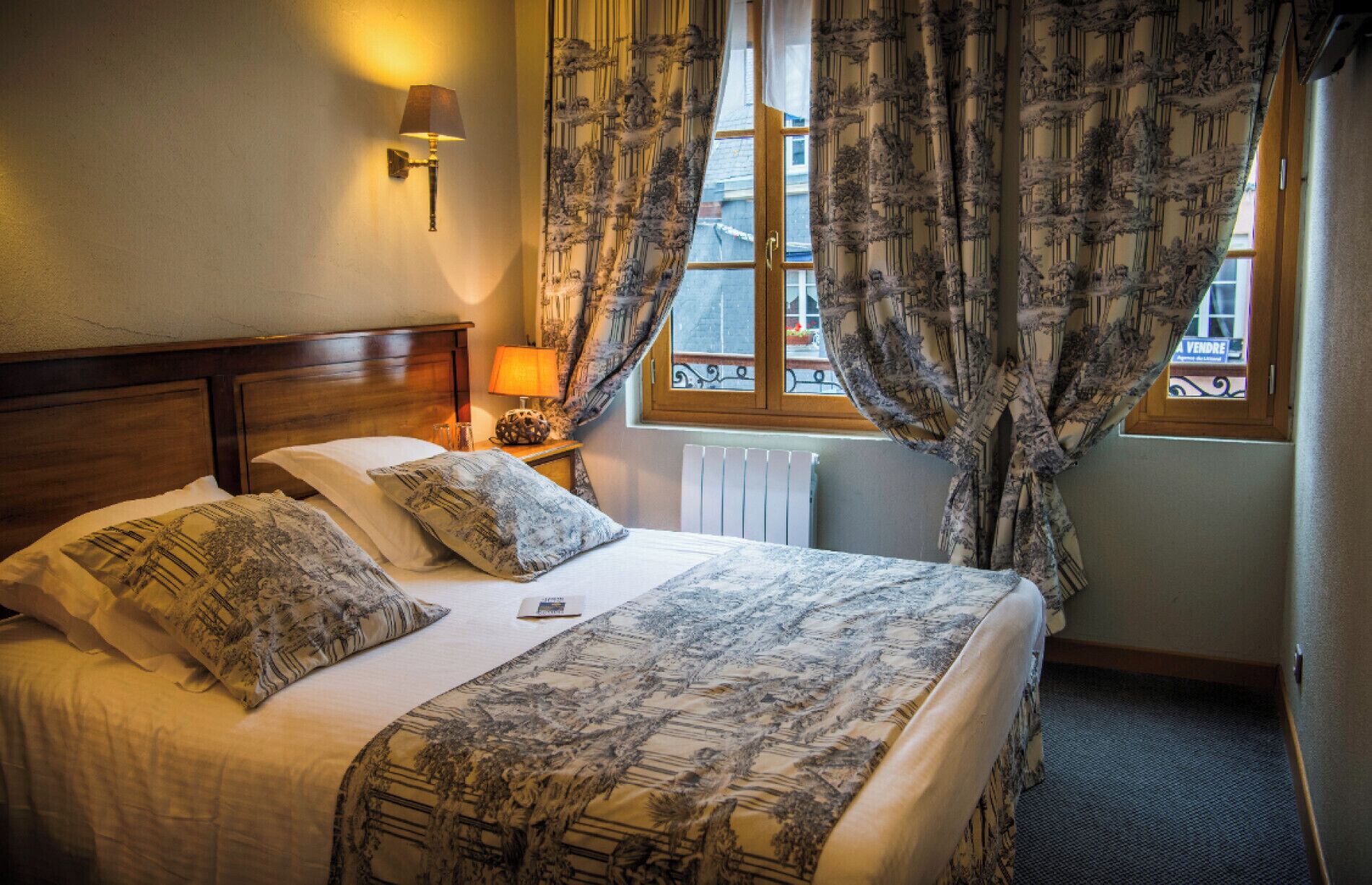 A neatly made bed with patterned bedding, a bedside lamp, and a window with curtains.