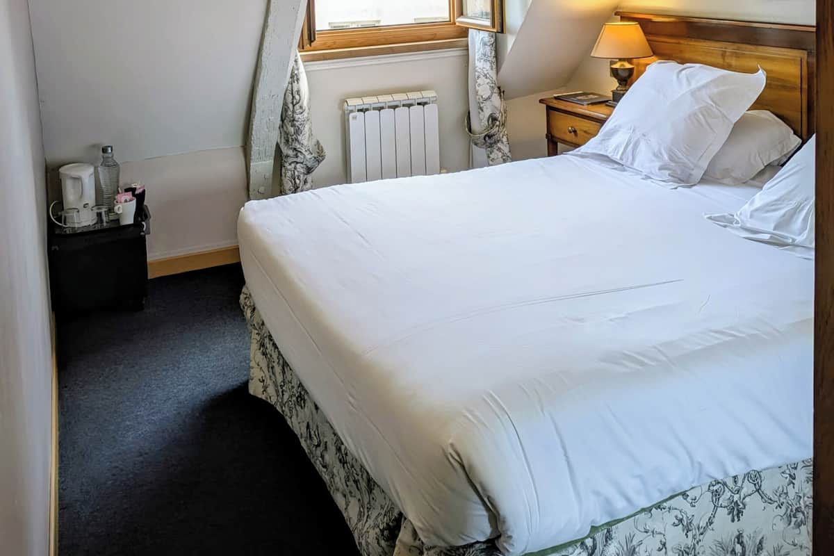 Une chambre à coucher avec un lit, une table de chevet, une lampe, un radiateur et une fenêtre.