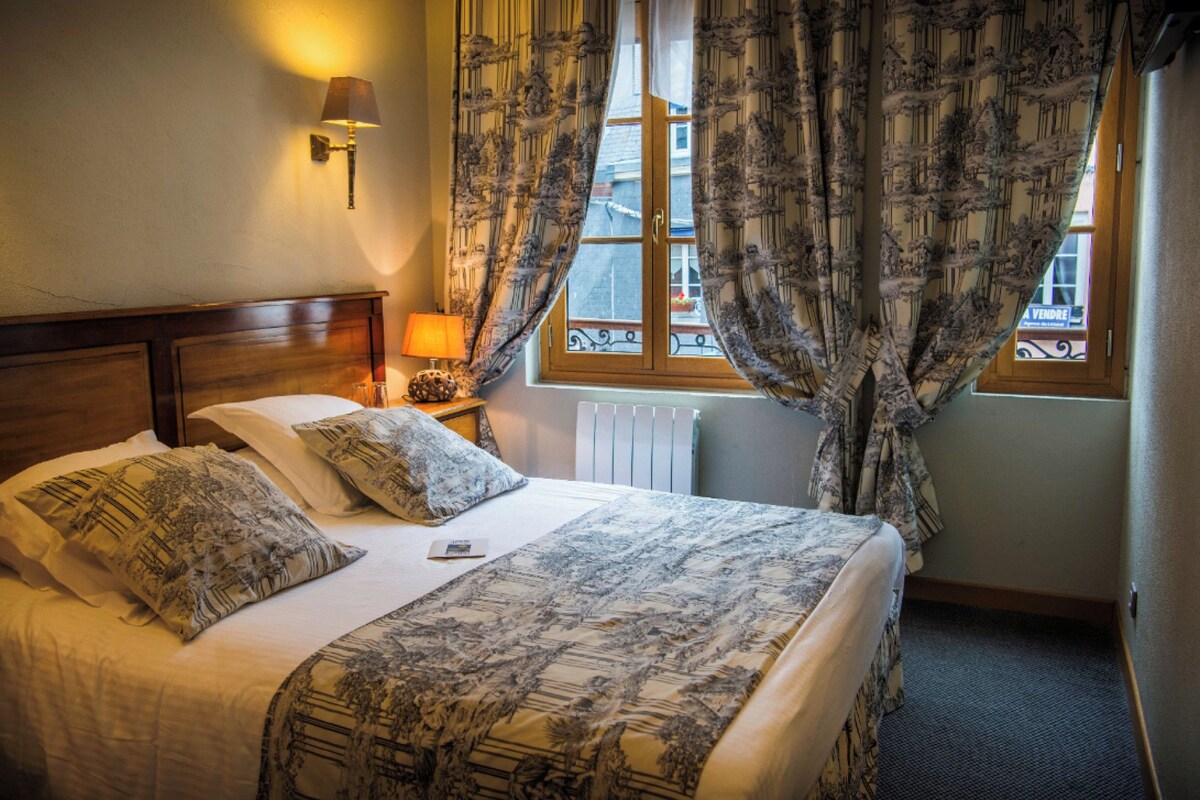 A neatly made bed with patterned bedding, a bedside lamp, and a window with curtains.