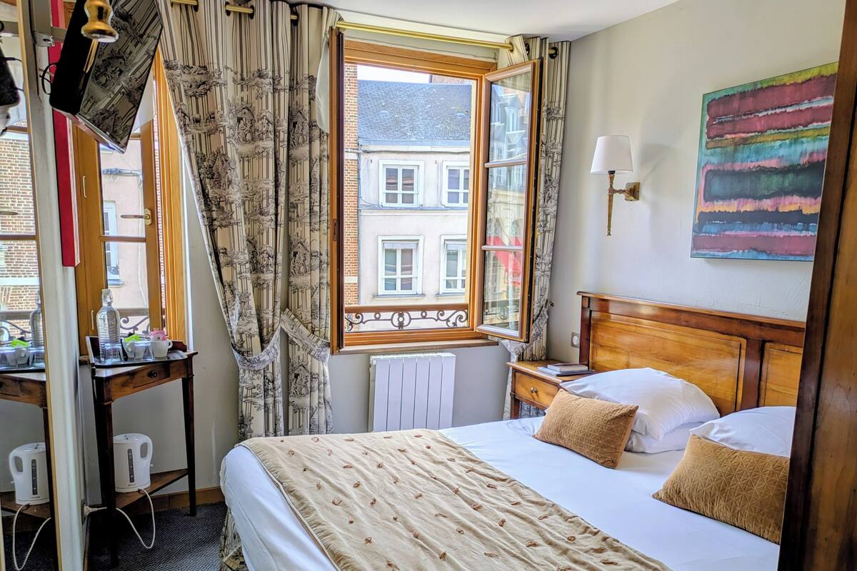 Une chambre d’hôtel avec un lit, un bureau doté d’une bouilloire, un radiateur et une fenêtre avec des rideaux.
