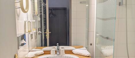 Un baño con tocador de madera, un lavabo blanco, cabina de ducha de cristal y un espejo sobre el lavabo.
