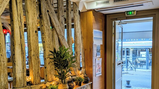 A stone wall with a wooden shelf holding plants and decorative items, a wooden slat wall, and a door leading outside. - Hôtel Entre Terre et Mer (Honfleur)