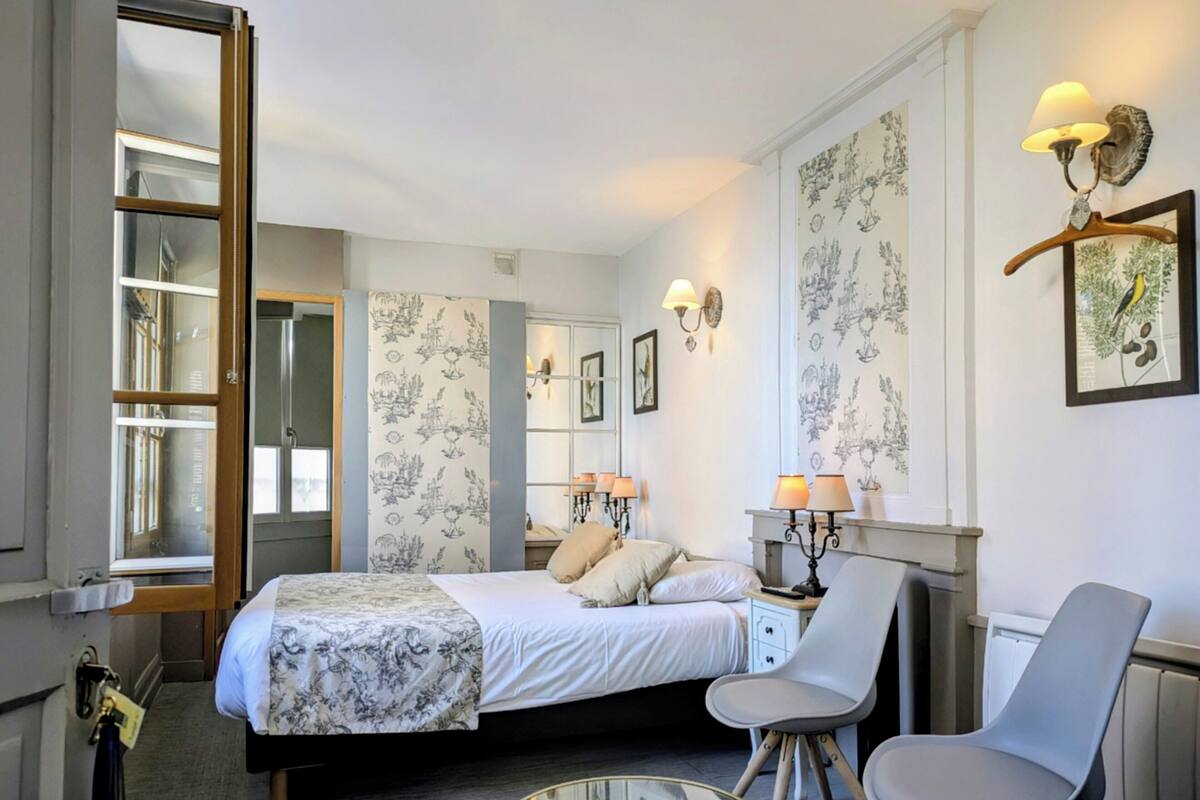 Une chambre d’hôtel avec un lit, une chaise, une table, une commode et un miroir.