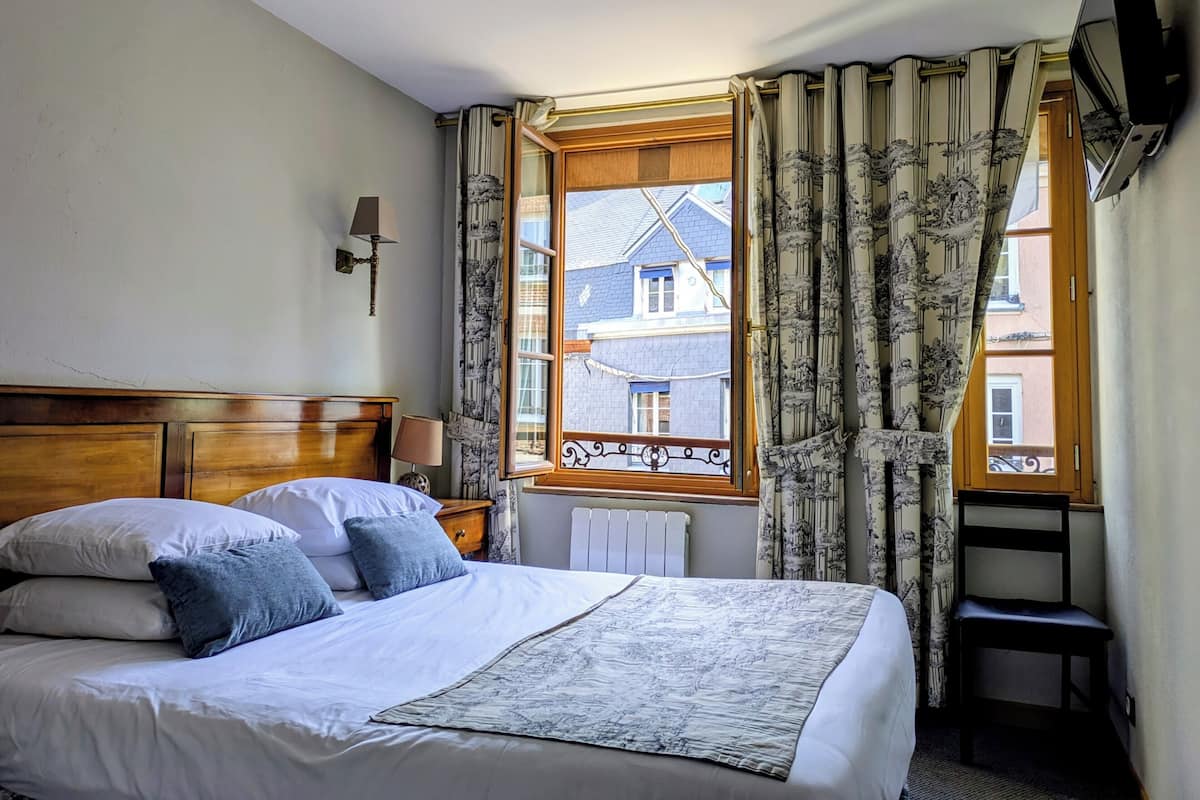 Une chambre d’hôtel comprenant un lit, une table de chevet, une lampe, une fenêtre avec des rideaux et un téléviseur fixé au mur.