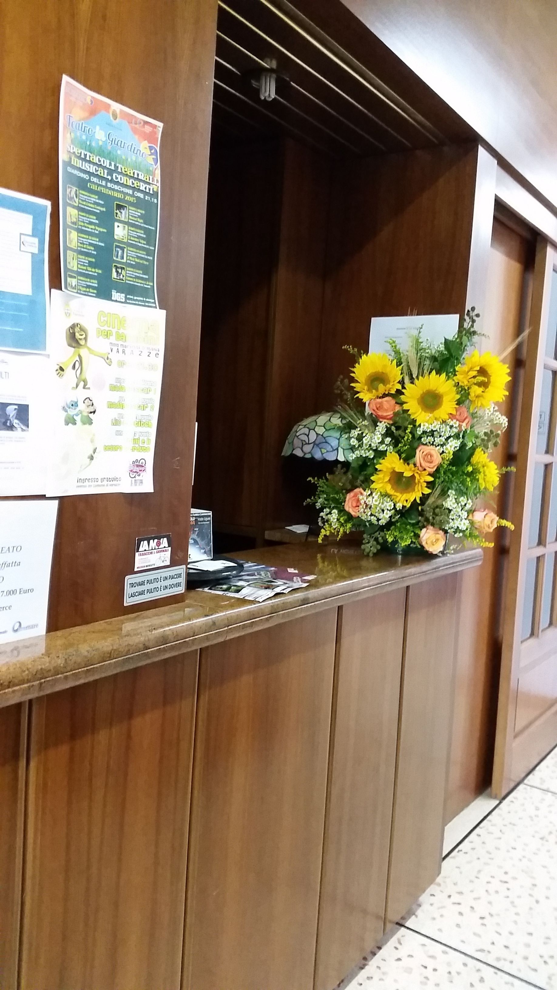 A wooden reception desk with a poster and a bouquet of sunflowers.