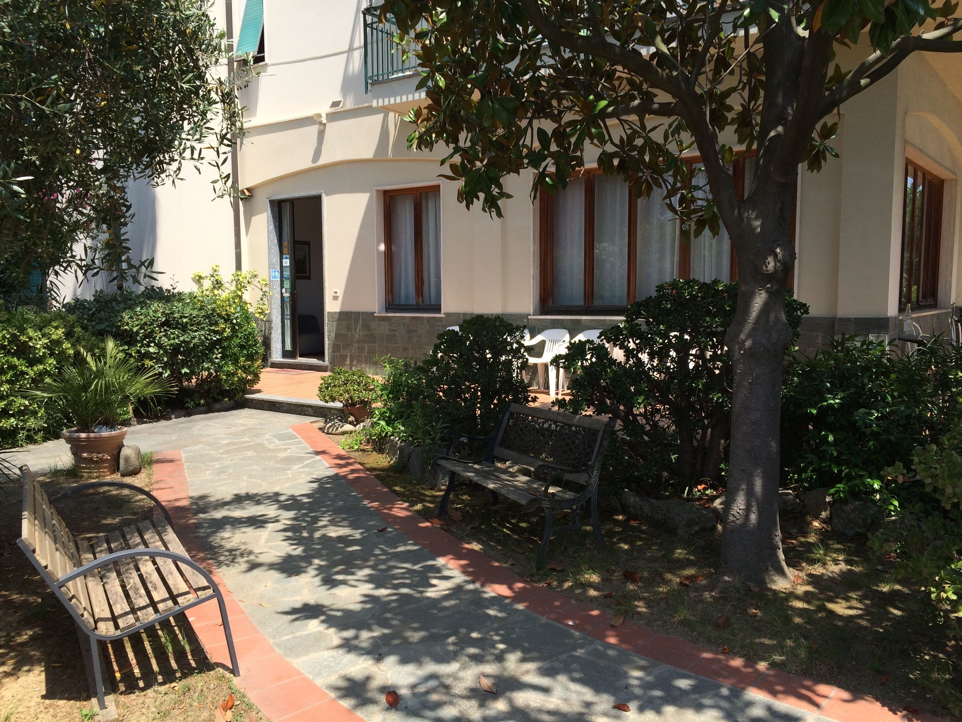 Une cour avec un banc, un arbre et un bâtiment doté d’une porte et de fenêtres.