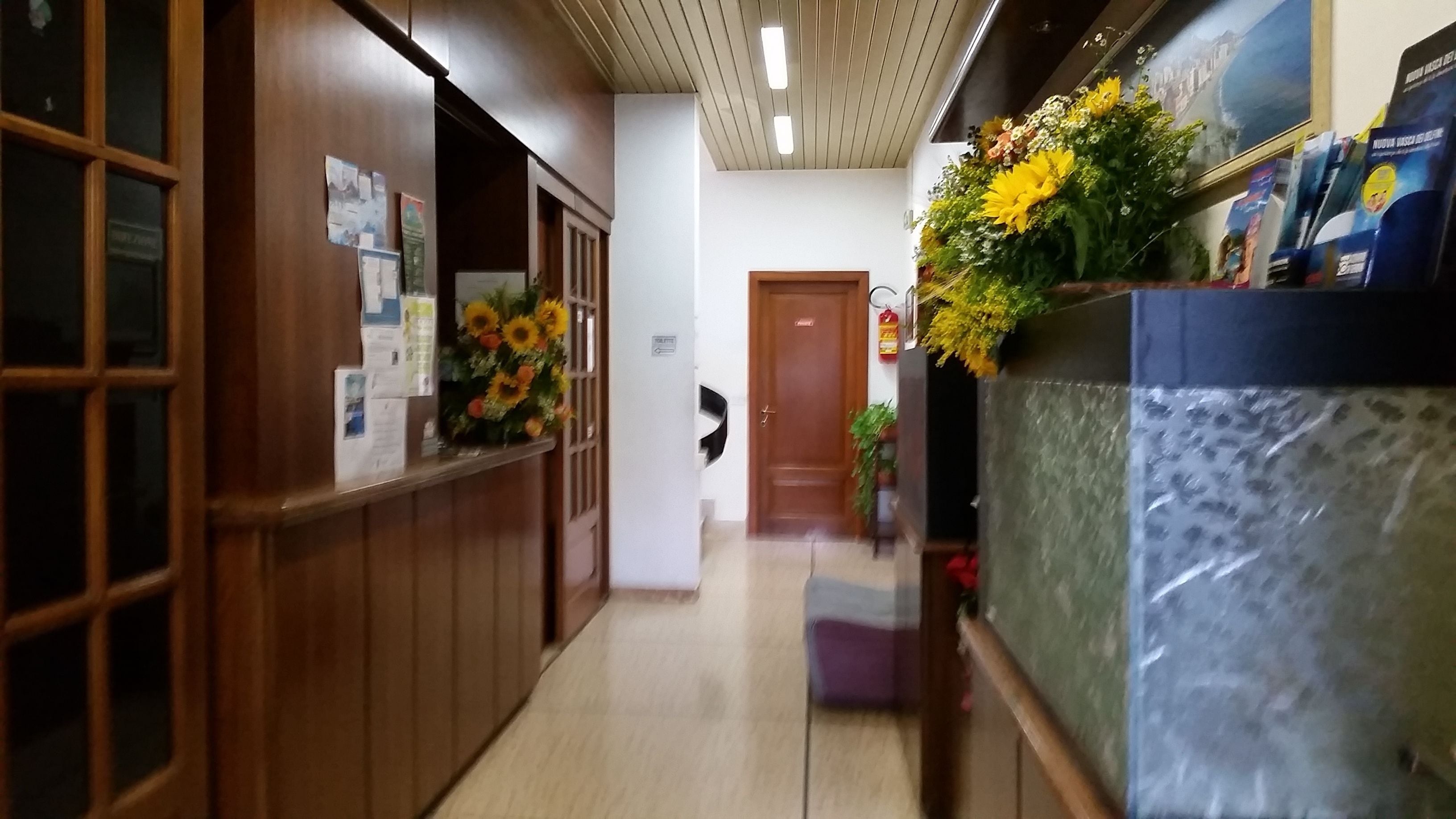 A hallway with wooden paneling, a reception desk with a floral arrangement, and a door in the background.