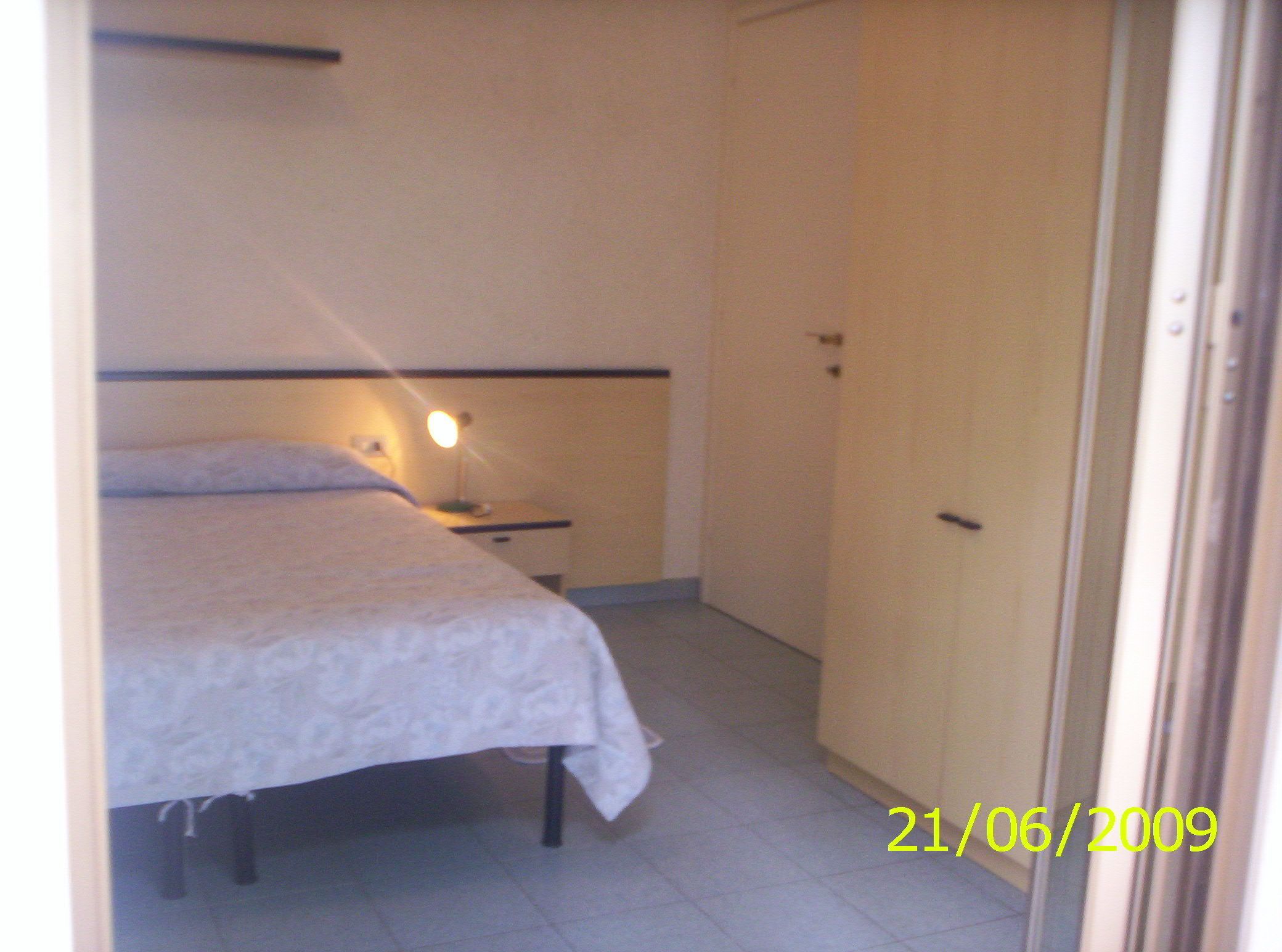 A small, single-bed room with a bedside table, a lamp, and a wardrobe.