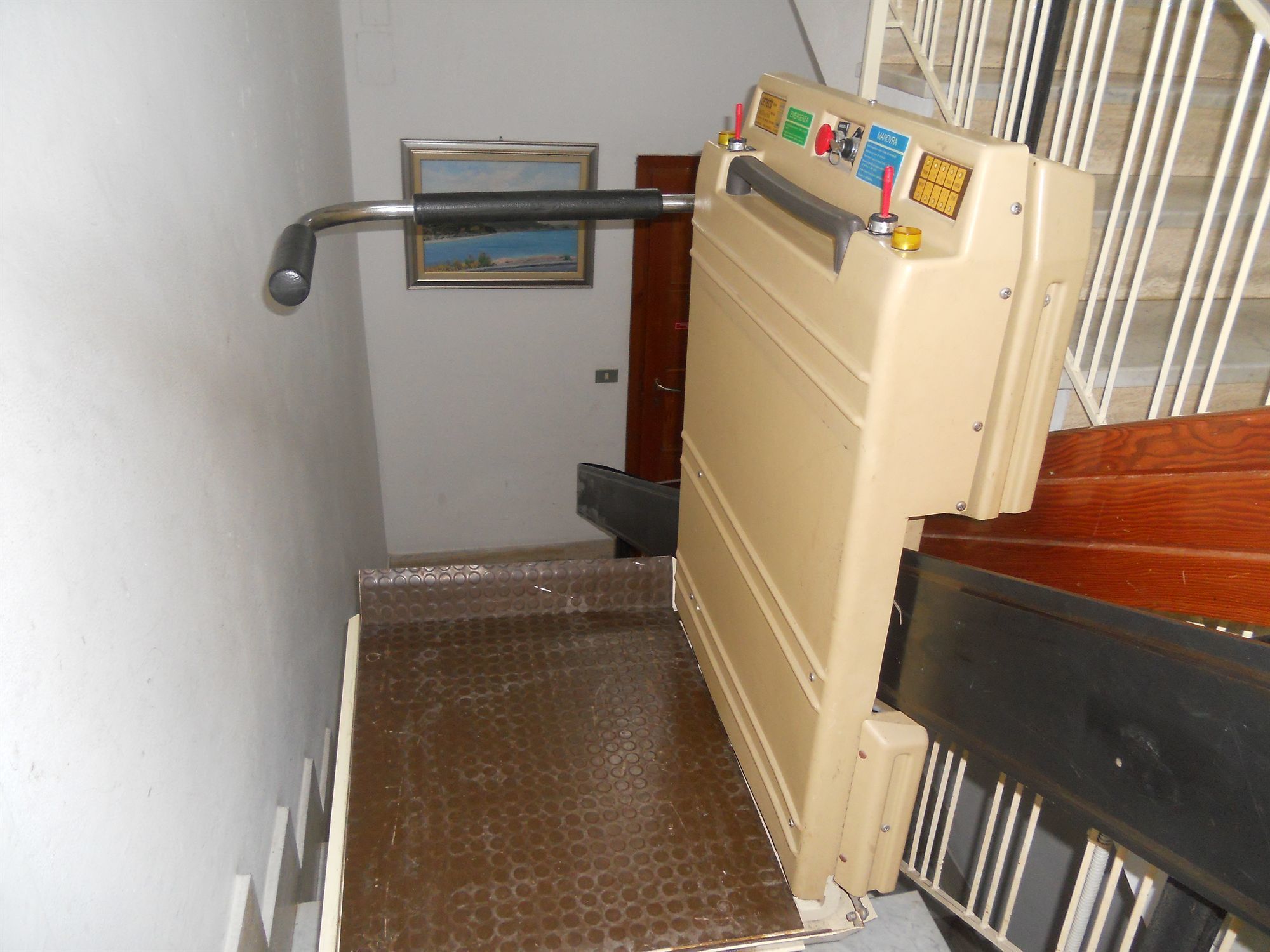 Un escalier doté d’une rampe métallique et d’un panneau de commande beige, muni de boutons et d’un écran.