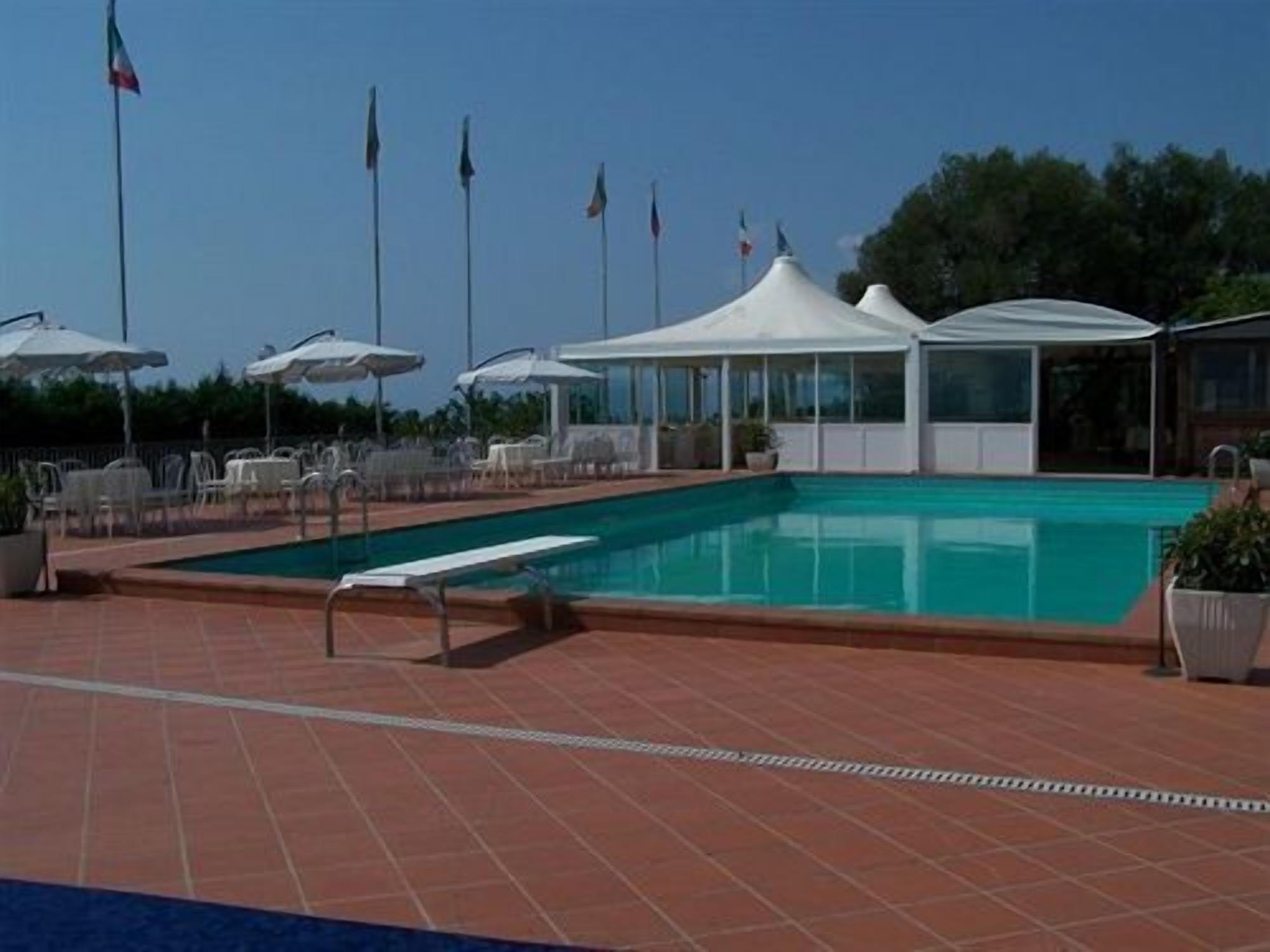 A swimming pool with lounge chairs and umbrellas, a covered seating area, and flags in the background.