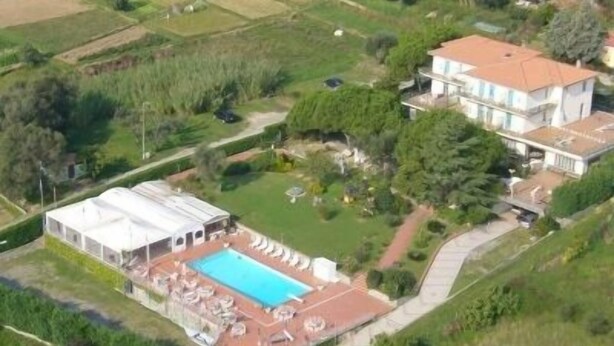 Vista aérea de una propiedad con una piscina grande, un invernadero y un edificio principal con techo rojo.