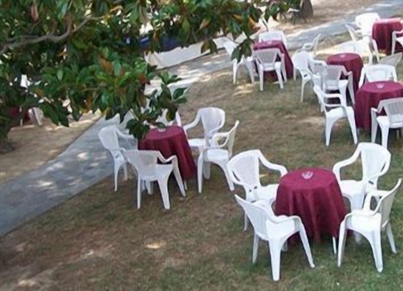 Mobiliario exterior con sillas y mesas de plástico blanco cubiertas con manteles rojos.