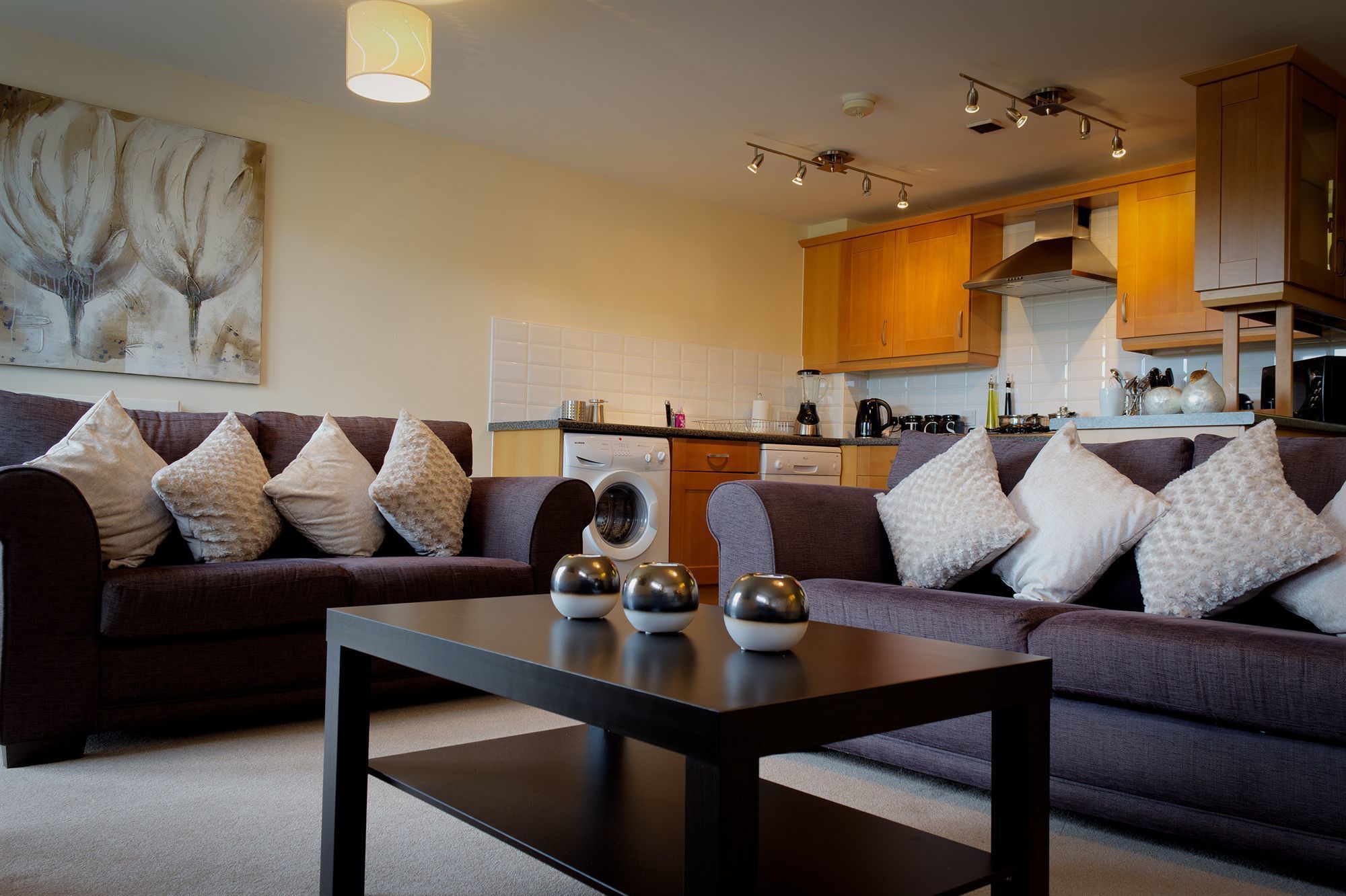 A modern living room with a dark brown sofa set, a black coffee table, and a painting on the wall.