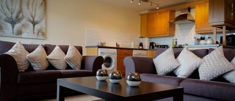 A modern living room with a dark brown sofa set, a black coffee table, and a painting on the wall.