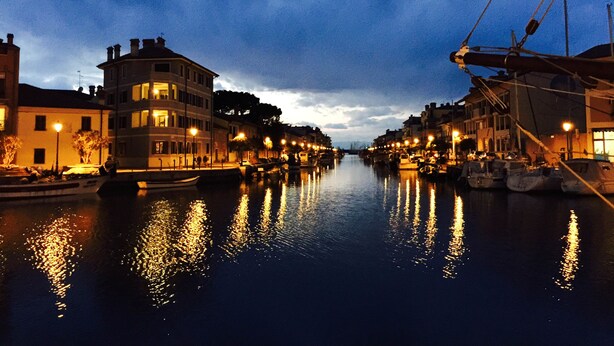 A canal with buildings on either side, boats docked along the water, and a clear sky. - Residence Hotel Hungaria (Grado)