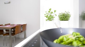 A dining area with a table and chairs, a plant on the windowsill, and a wok with vegetables. - Residence Hotel Hungaria (Grado)