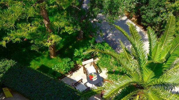 An aerial view of a lush garden with a paved patio area, surrounded by dense greenery and trees. - Golden Apartments (Agios Nikolaos)