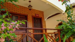 A brick building with a wooden balcony railing, a door with a number, and a hanging light fixture. - Pousada Jardim dos Orixás (Aracati)