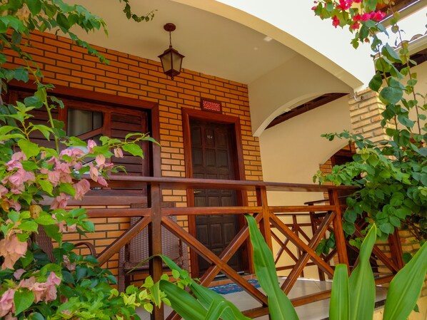 A brick building with a wooden balcony railing, a door with a number, and a hanging light fixture. - Pousada Jardim dos Orixás (Aracati)