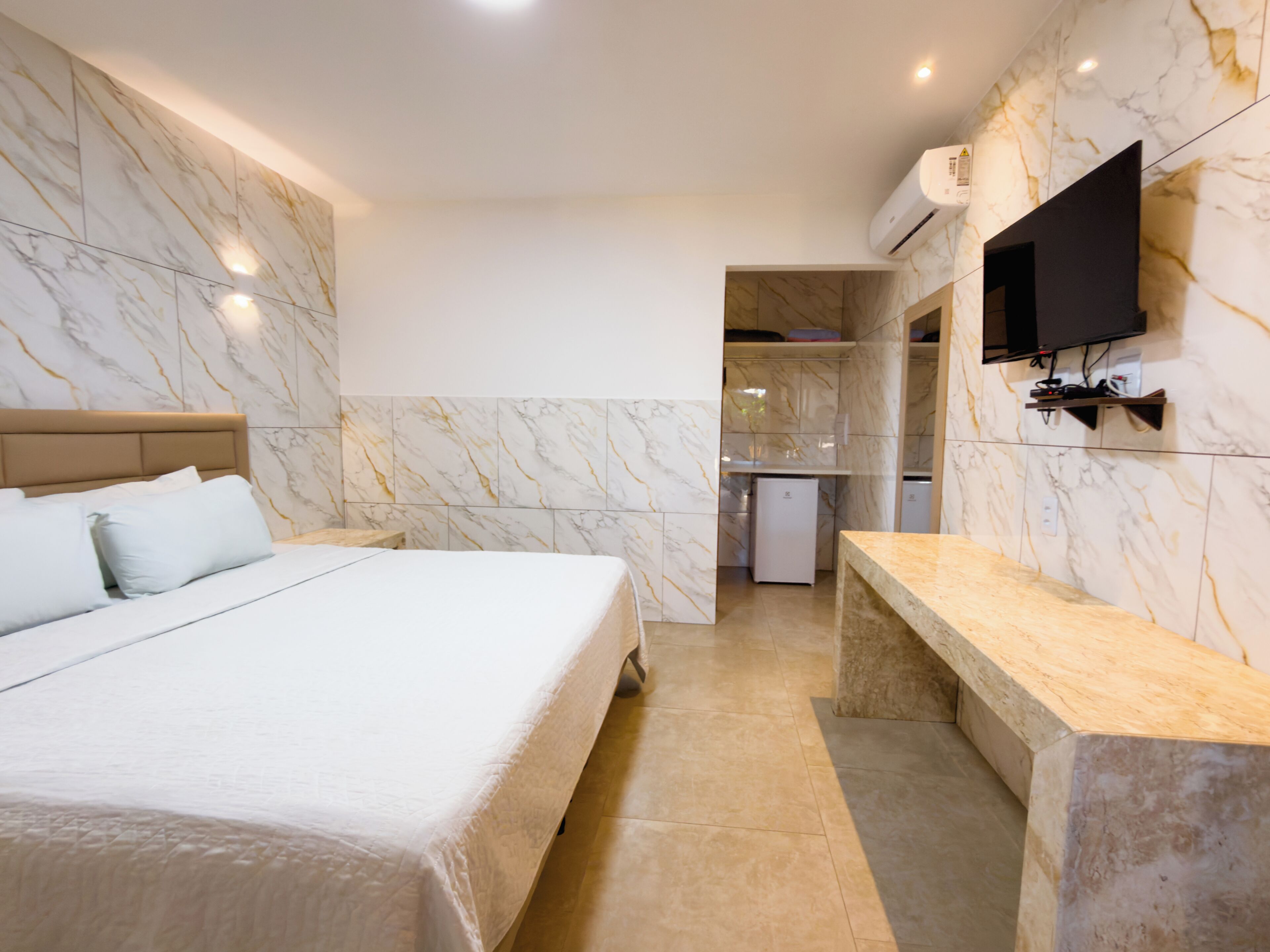 A hotel room with a bed, a bench, a TV, and a small kitchenette.