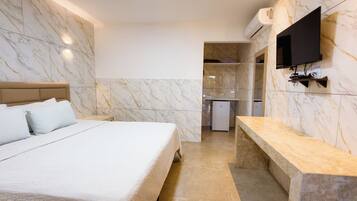 A hotel room with a bed, a bench, a TV, and a small kitchenette.