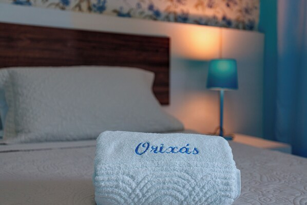 A neatly made bed with a white pillow and a folded towel with 'Orixás' embroidered on it. - Pousada Jardim dos Orixás (Aracati)