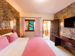 A hotel room with a bed, a TV, a desk, and a view of the outside. - Pousada Jardim dos Orixás (Aracati)