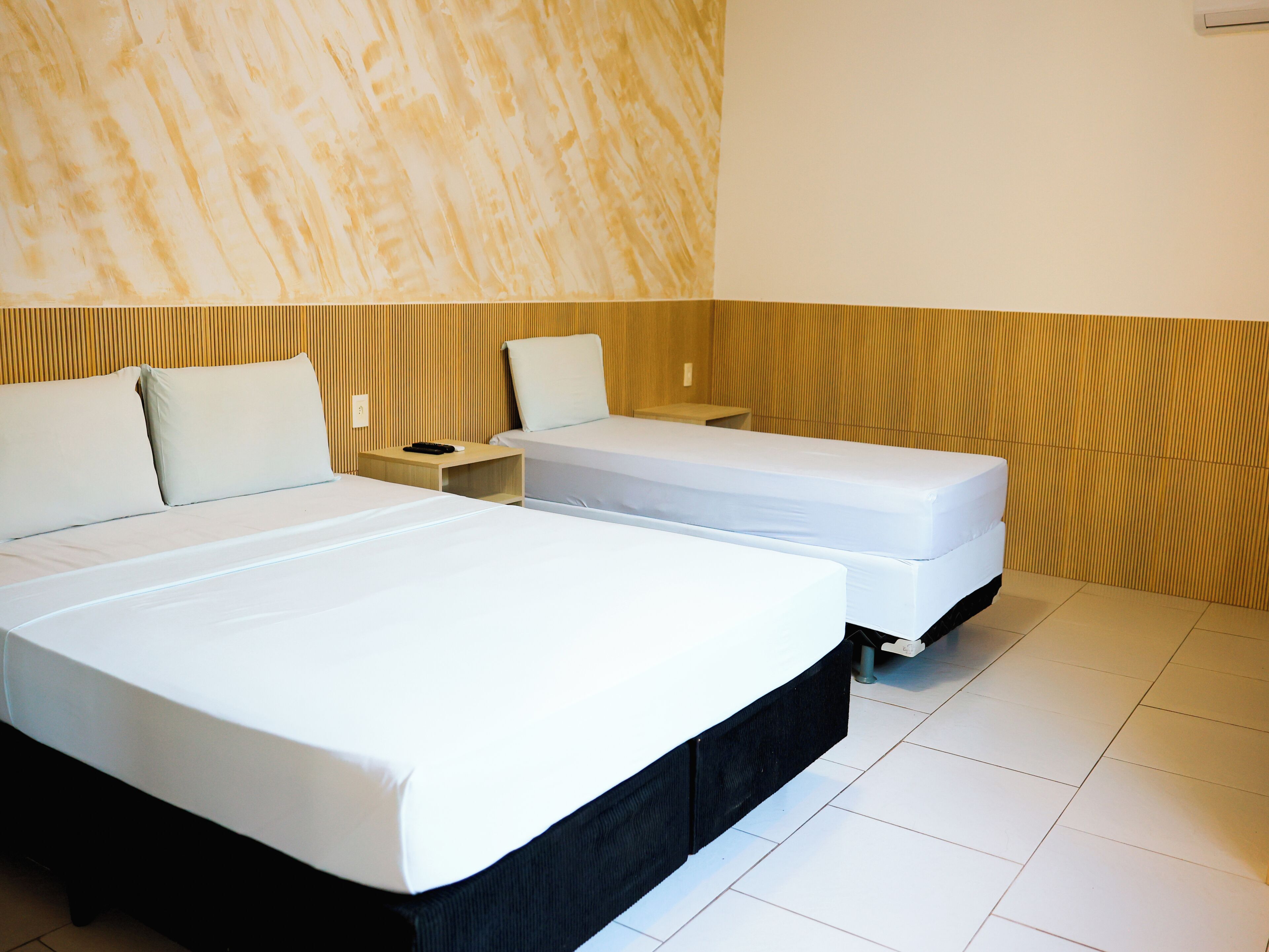 A hotel room with two beds, a wooden headboard, a nightstand, and a white tiled floor.
